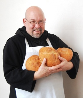 Father Dominic, the Bread Monk, holding several loaves of bread