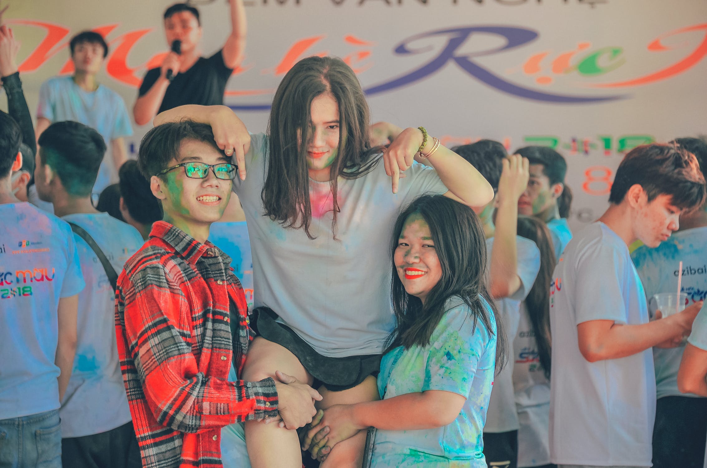 Two teens holding up a third teen. All three are covered in colorful paint. 