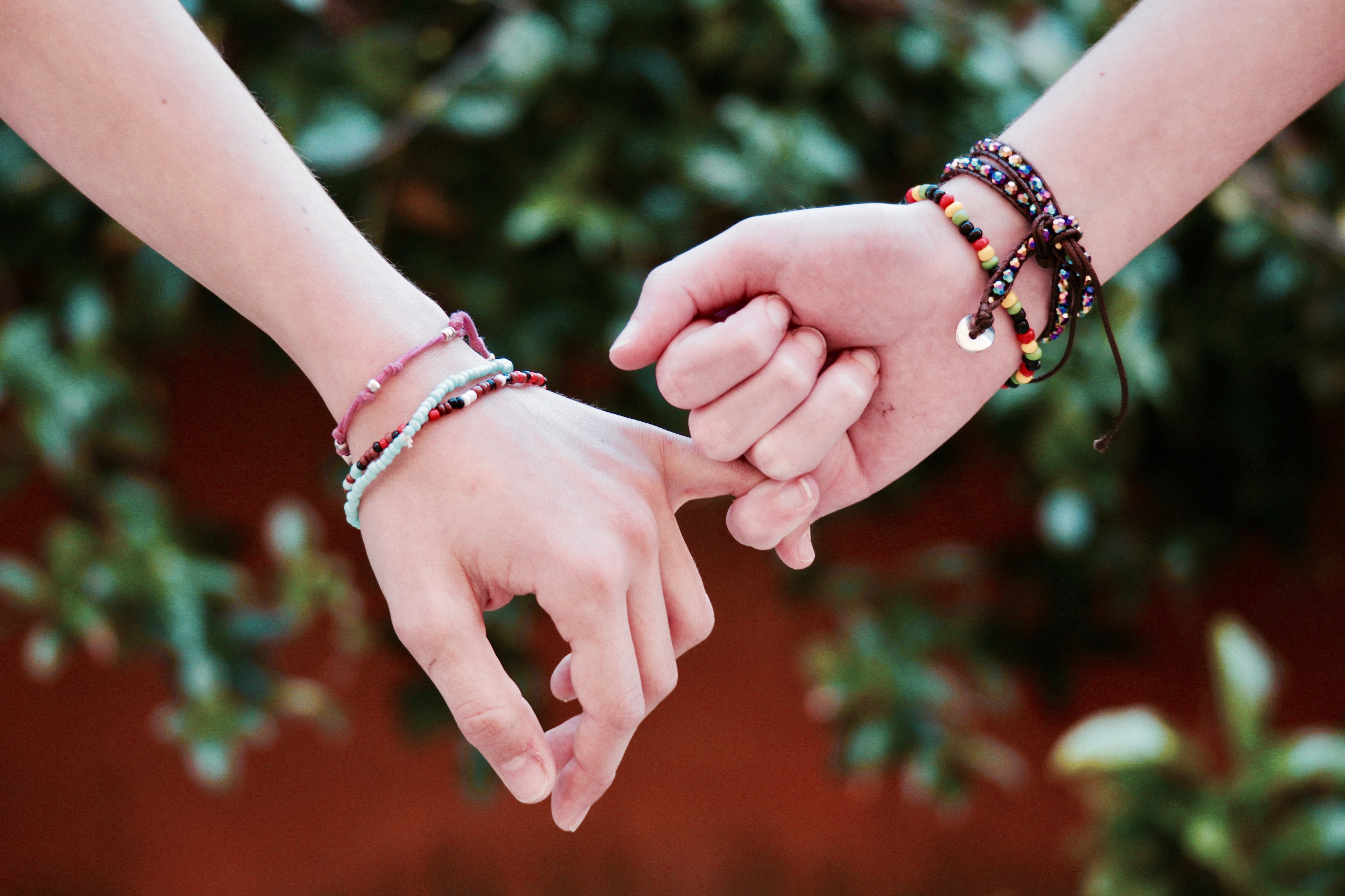 two people wearing friendship bracelets, holding hands 