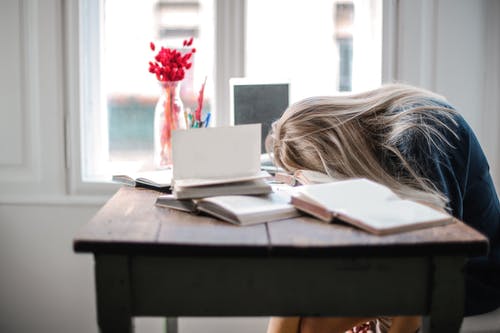 A girl sits at a desk with her head on top of an open book.