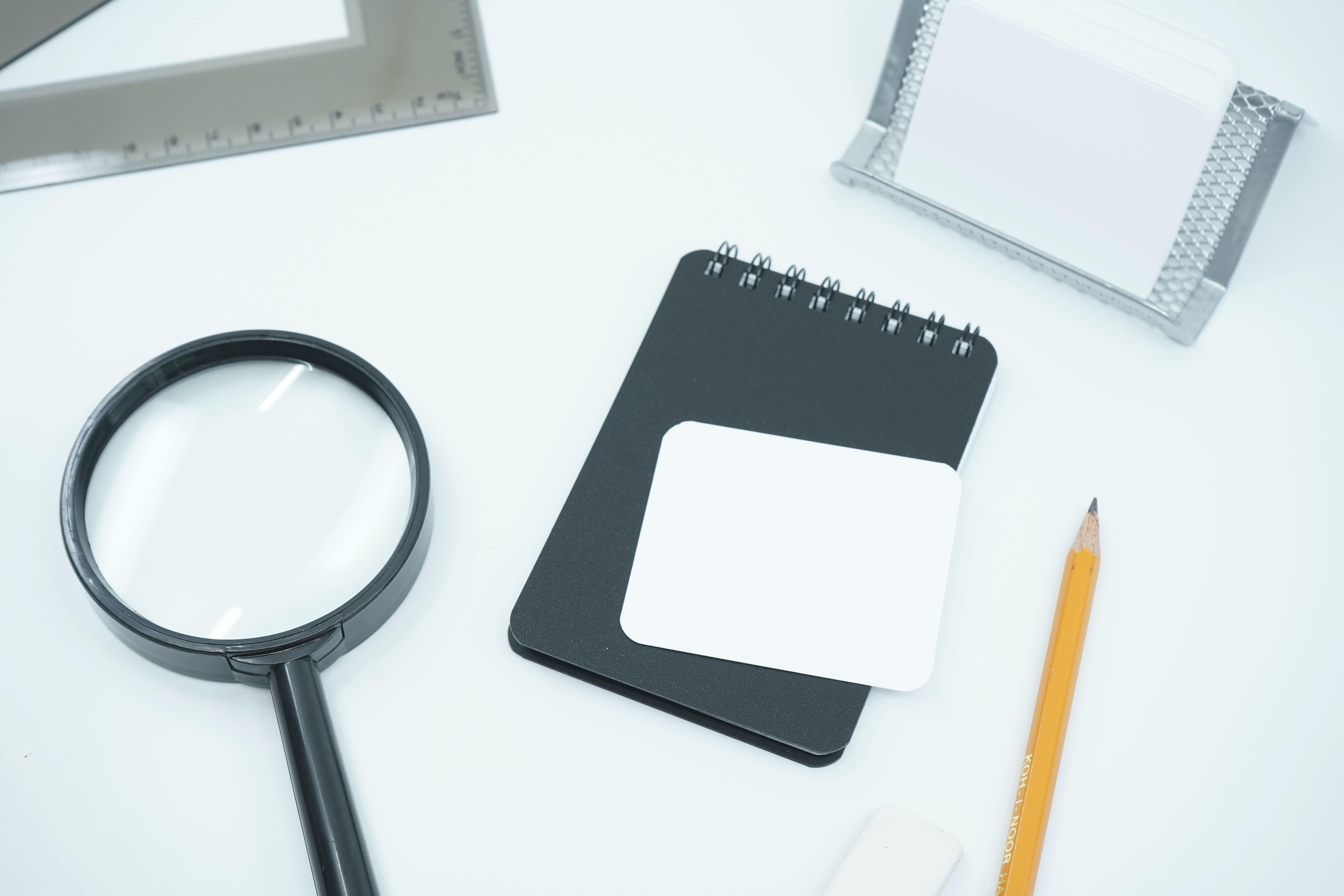 A white background with a magnifying glass, notebook, and yellow pencil.