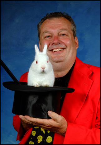 A man in a red jacket holds a black top hat. A white rabbit sits inside the hat. 