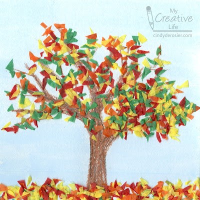 A light blue background with a large brown tree. The tree's leaves are made of orange, red, yellow, and green tissue paper.