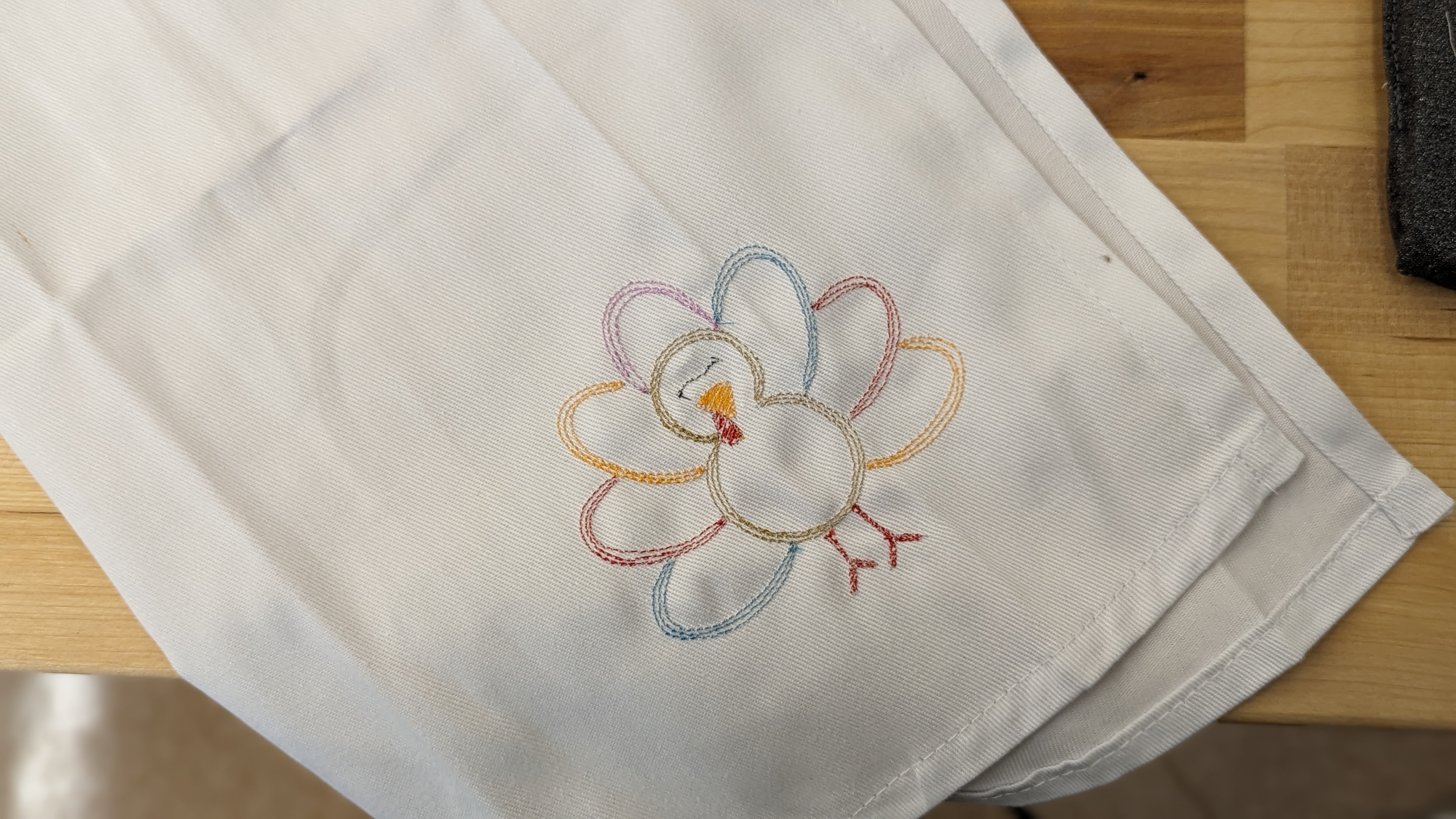 Image of cloth napkin embroidered with a multi-color design in the shape of a turkey