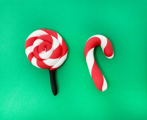 Red and white air dry clay lollipop and candy cane on green background