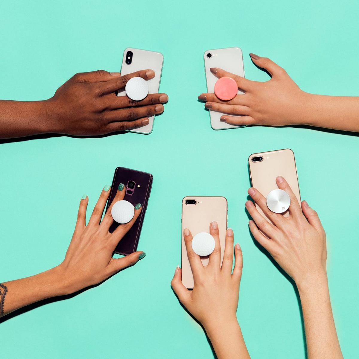 Hands holding cell phones with pop sockets attached to them. 